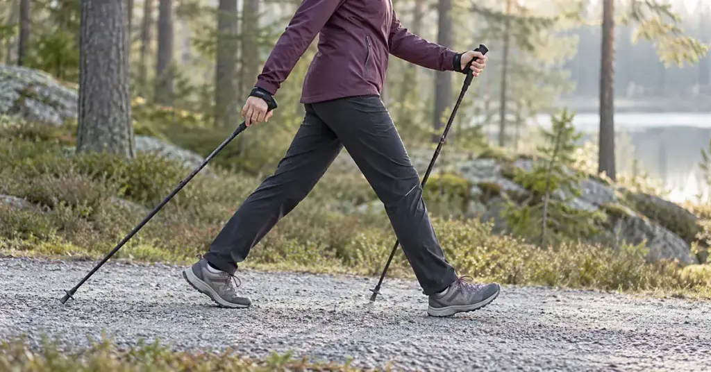 Sauvakävelijä askeltaa metsäisellä sorapolulla sauvat taaksepäin kallistettuina.